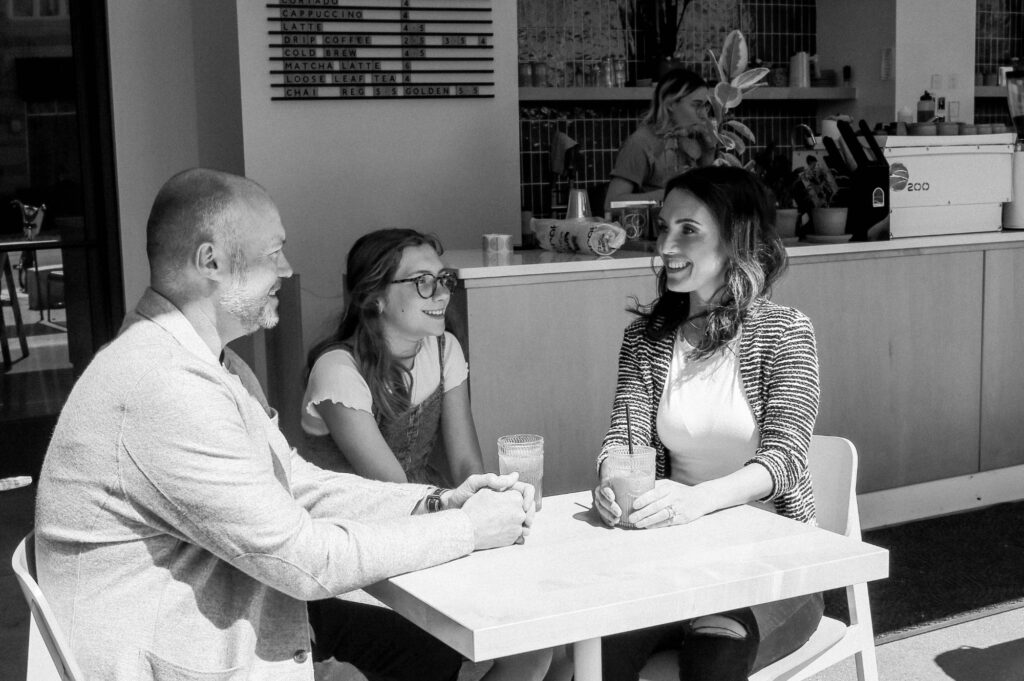 Mindy talks with a father and daughter in a cafe.